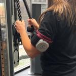 A woman is wearing a BFR cuff while performing low weight rope pull downs at Synergy Physical Therapy